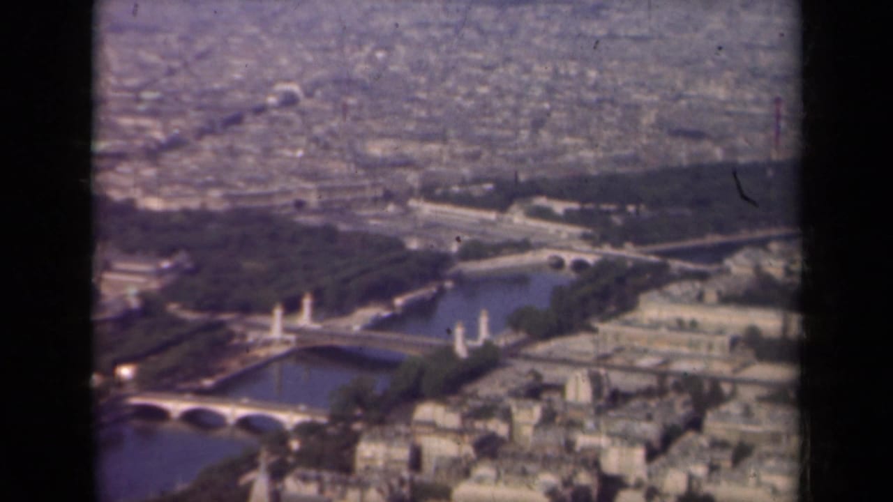 Aerial view over a river bend, bridges, trees, and city buildings.