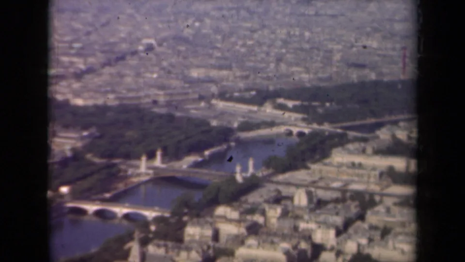 1939 Paris aerial frame showing Seine bridges, riverside trees, open park areas, and surrounding urban blocks in grainy 8mm color.