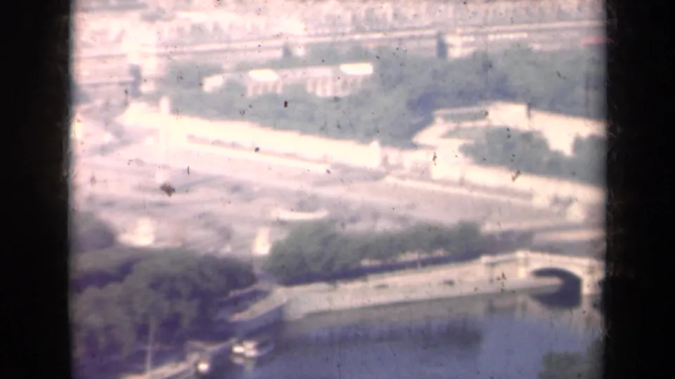 Overexposed 1939 Paris aerial frame with a Seine bridge, bright formal grounds, tree masses, and river water near the lower edge.