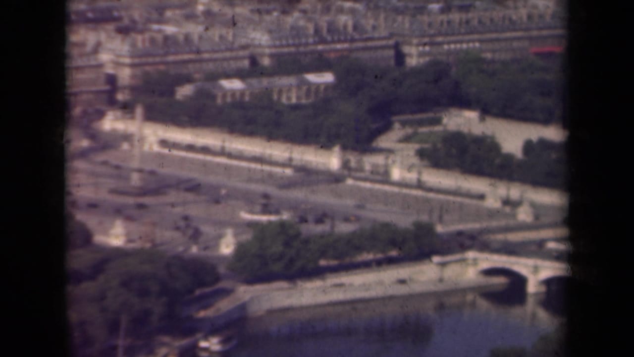1939 Paris aerial frame with the Seine, arched bridges, fountains, formal gardens, and dense city blocks in soft 8mm color.