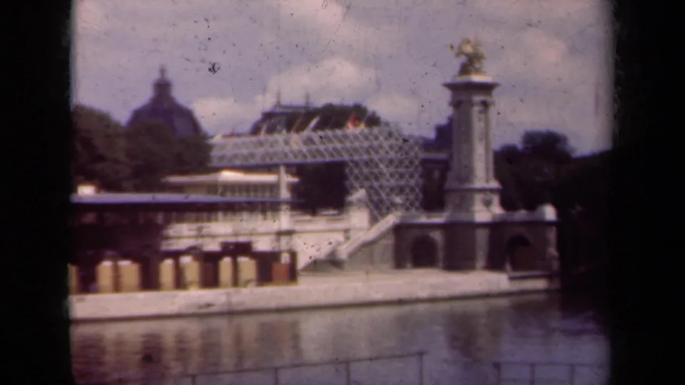 1939 Paris frame showing a waterside monument, gilded statue, pale arched structure, dark trees, and distant dome.