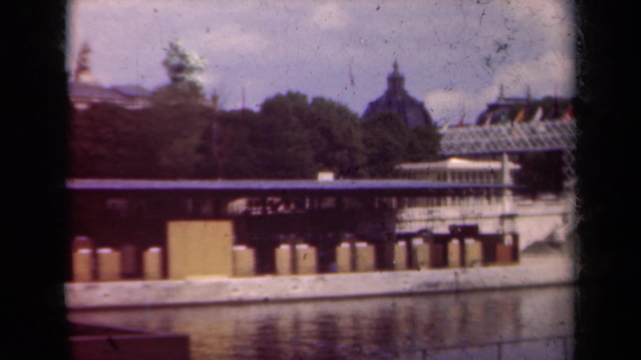 Riverside view with trees, a long dock, water reflections, and a distant domed building.