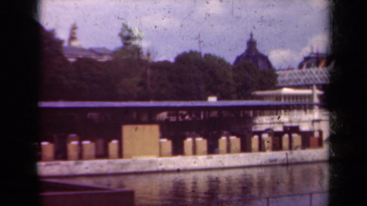 Similar riverfront view with dock posts, trees, water, and a domed building in the distance.