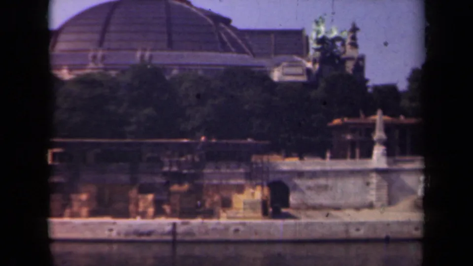 1939 Paris home-movie frame with a domed structure, decorative rooftop sculpture, trees, and a stone waterfront edge.