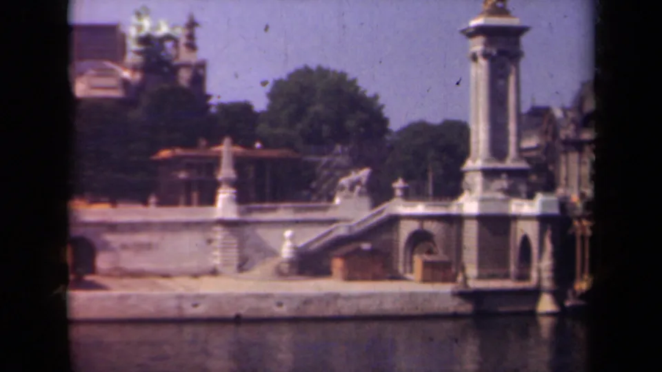 1939 Paris home-movie frame of a classical riverside structure with steps, a column, arched doorway, and trees behind.