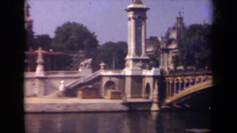 1939 Paris frame with ornate bridgework at right, stone riverfront stairs, a tall column, trees, and a distant dome.