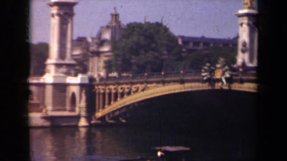 1939 Paris home-movie still showing the ornate bridge from a slightly shifted angle, with distant pedestrians near the railing and water below.