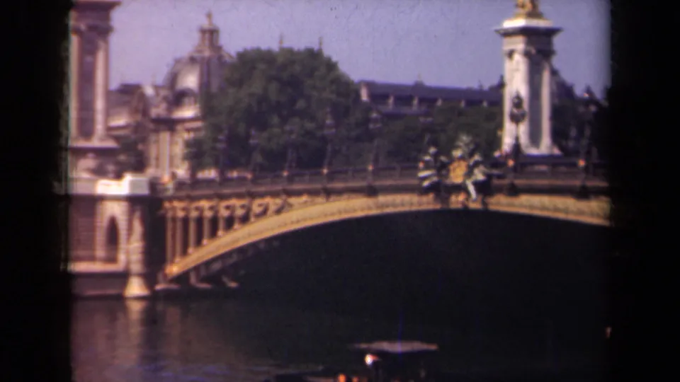 1939 Paris 8mm frame showing Pont Alexandre III spanning the Seine, with decorative columns, distant buildings, and a small boat on the river.