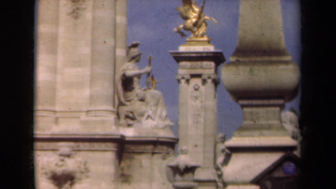 Close 1939 Paris view of Pont Alexandre III decorative stonework, including a seated figure sculpture and gilded winged ornament against the sky.