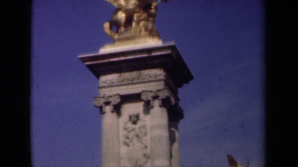 1939 Paris home-movie frame showing the gilded winged horse sculpture more prominently above a carved stone pedestal with ornamental reliefs.