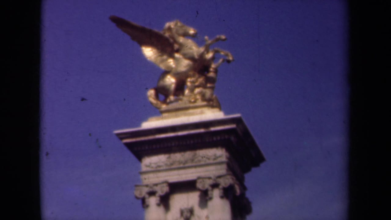 1939 Paris 8mm frame showing a gilded winged horse sculpture atop a classical stone pedestal against deep blue sky.