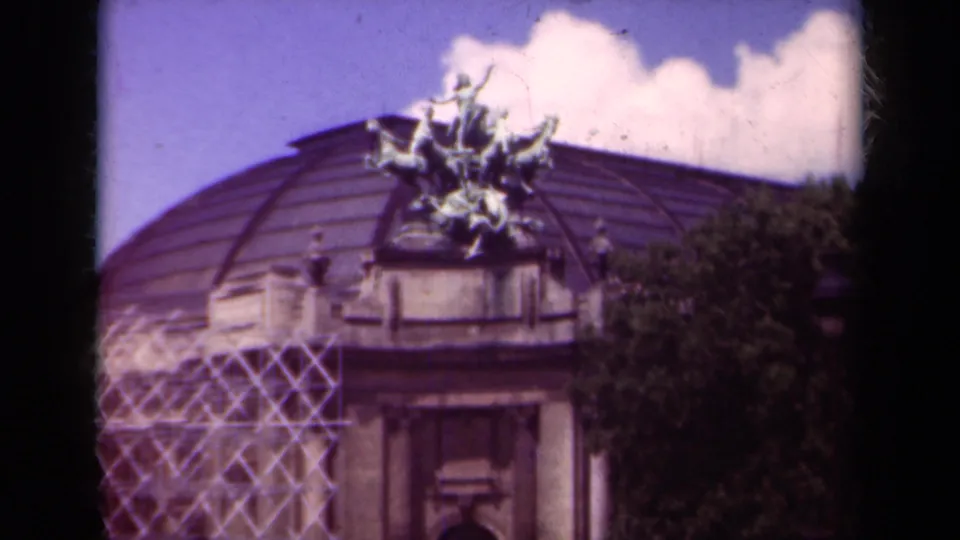 1939 Paris 8mm frame with a wider view of a domed building, rooftop sculpture, scaffolding, and clouds.