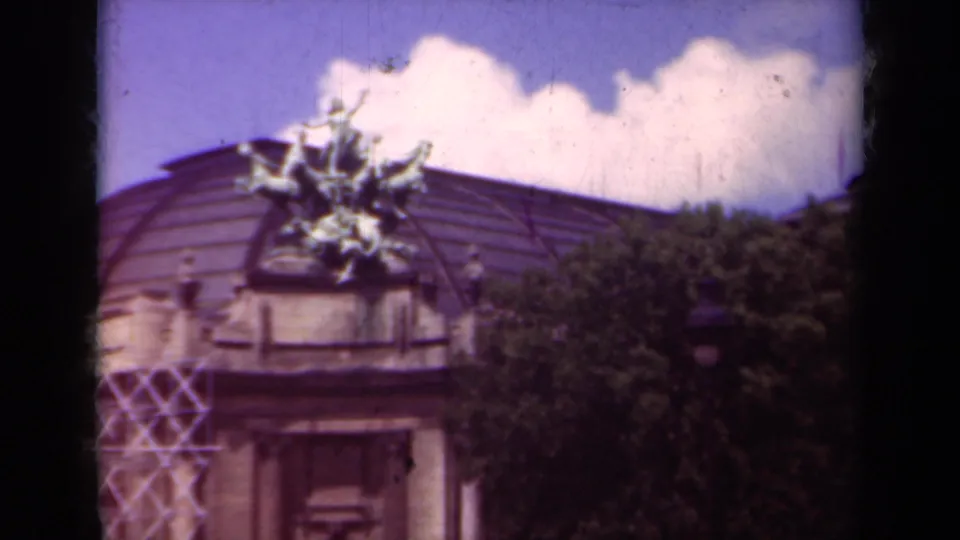 1939 Paris 8mm frame showing a domed landmark-like facade with rooftop sculpture, tree foliage, and clouded sky.