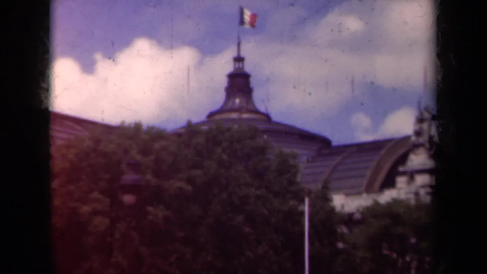 A soft 8mm Paris frame shows the flag-topped dome, roofline, trees, and a partial ornate facade at the right edge.