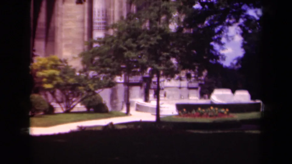 A soft 8mm view of a Paris formal building framed by trees, lawn, a pale walkway, and a planted border.