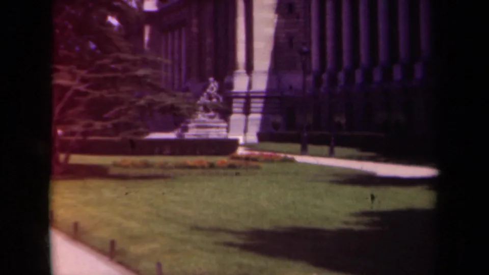 1939 Paris 8mm frame showing a manicured lawn, statue, walkway, and the side of a grand neoclassical building.