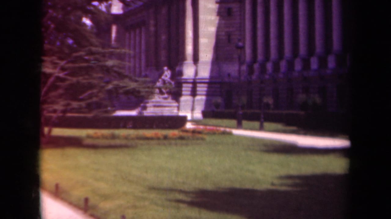 1939 Paris 8mm frame showing a classical building facade with columns, a formal garden lawn, flowerbed, path, and central sculpture.