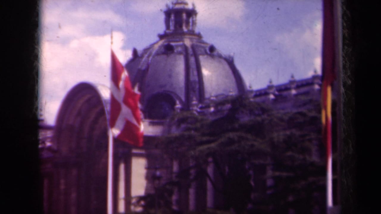 1939 Paris frame with the Swiss flag centered near a flagpole, an ornate dome behind it, trees below, and soft 8mm color.