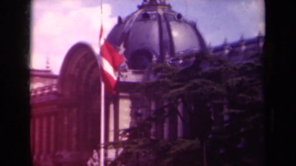 1939 Paris frame showing the Swiss flag in breeze before classical columns, an arched section, domed roof, and dark foreground trees.