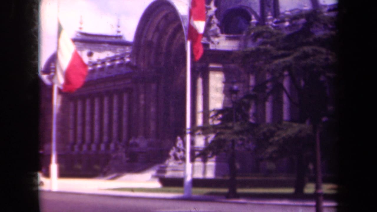 1939 Paris street view of a formal stone building with French flags, trees, and a broad roadway in front.