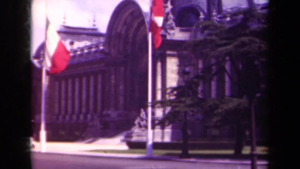 1939 Paris street view of a formal stone building with French flags, trees, and a broad roadway in front.