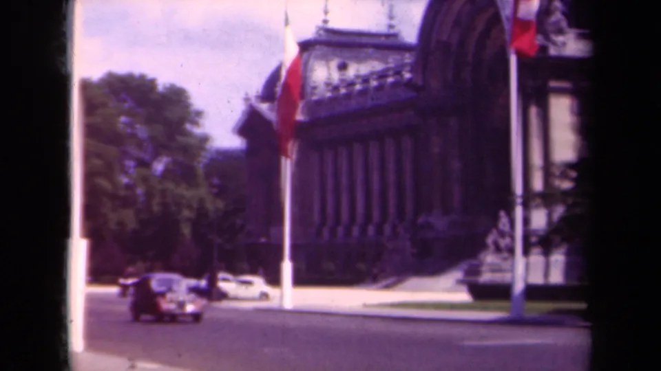 1939 Paris street scene with classic cars, a tall flagpole, trees, and part of a grand stone building.