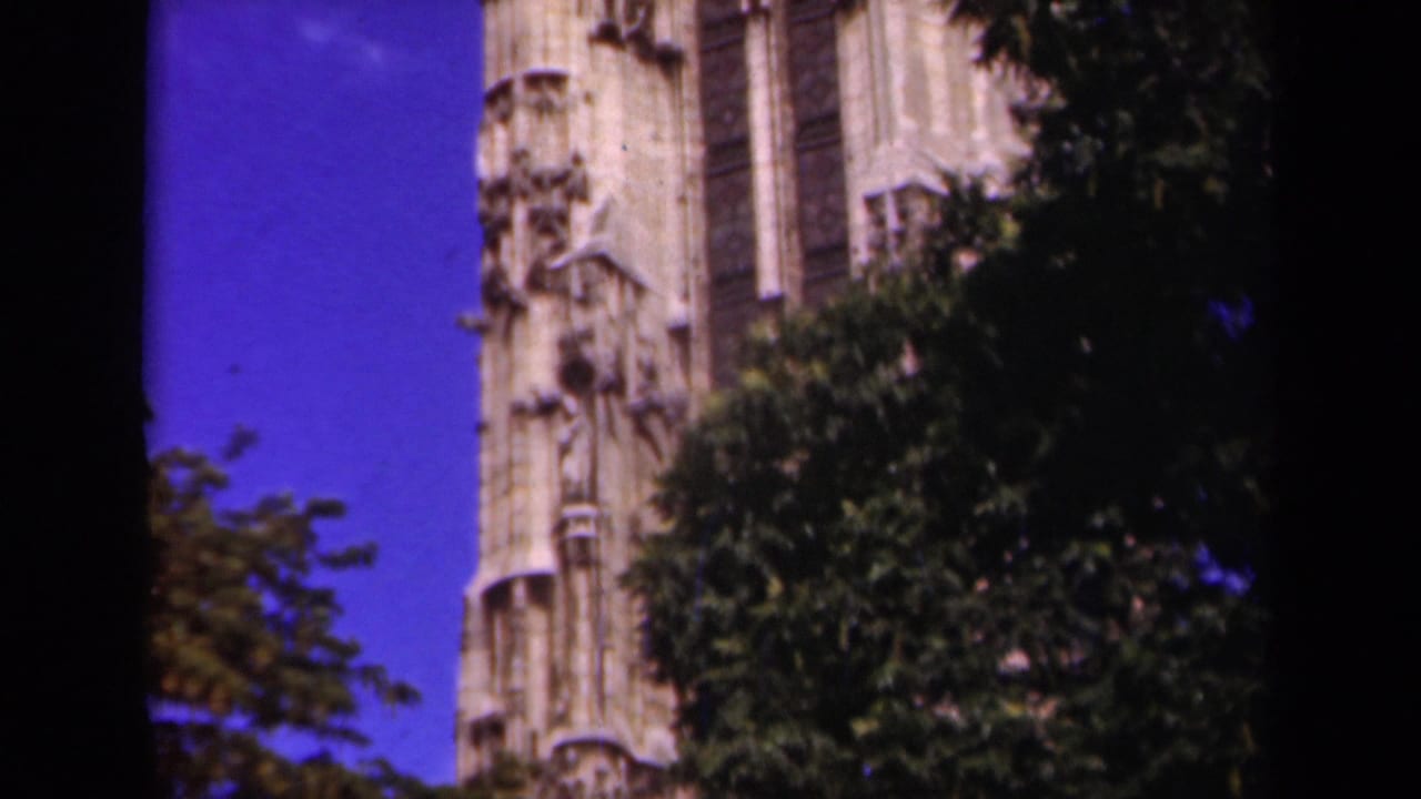 1939 Paris 8mm frame showing the lower portion of a Gothic cathedral tower partly obscured by leafy branches.