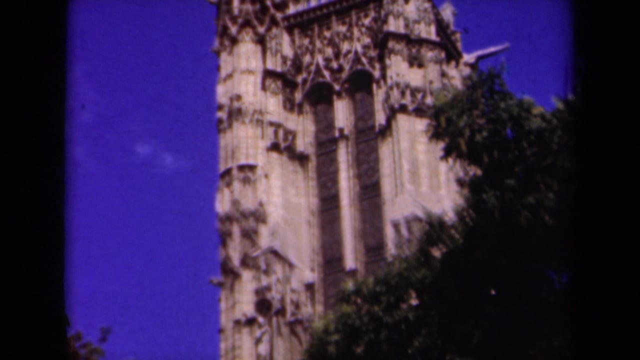1939 Paris 8mm frame with ornate Gothic cathedral stonework, tree cover, and a strong blue-purple sky.