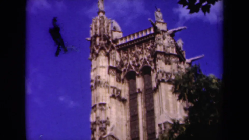 1939 Paris 8mm frame showing the upper cathedral facade with Gothic tracery, small spires, and tree branches at the edge.