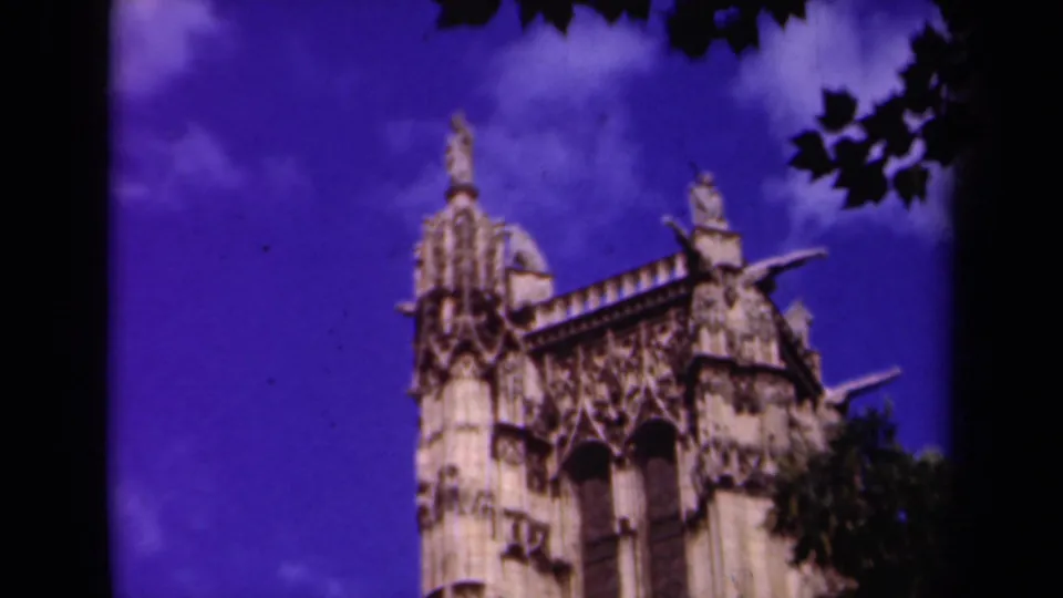 1939 Paris 8mm frame showing the cathedral's upper stone facade and spires against a blue-purple sky, with leaves intruding at right.