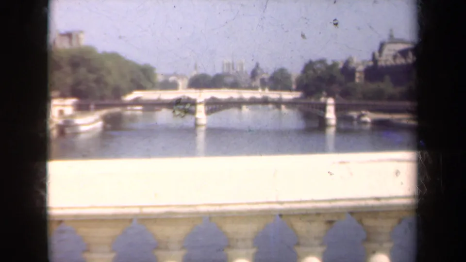 1939 Paris 8mm river view across the Seine, with a stone bridge, tree-lined banks, and cathedral forms in the distance.