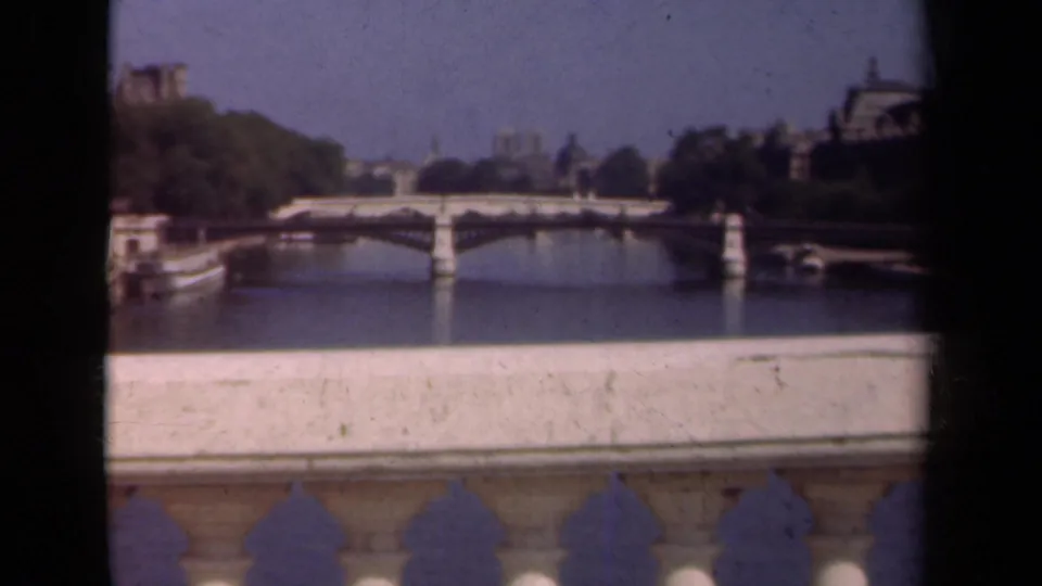 1939 Paris view of a Seine bridge and distant Notre-Dame, framed by trees, buildings, and a foreground parapet.
