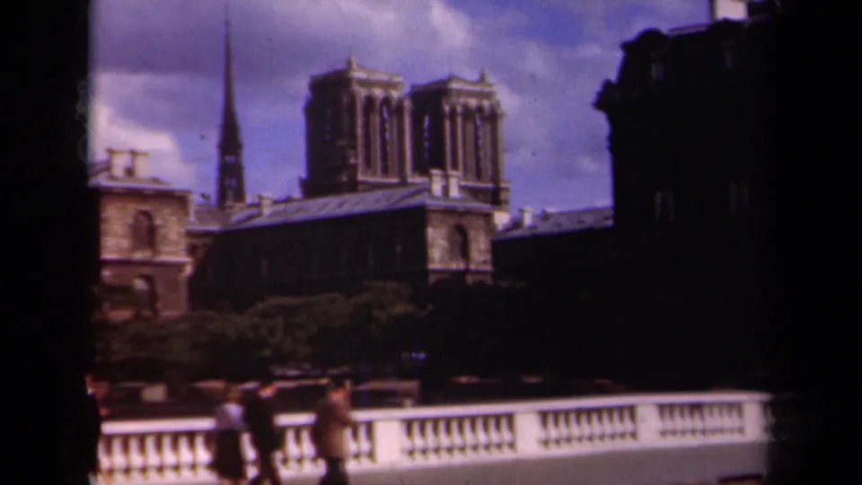 1939 Paris footage showing Notre-Dame Cathedral towers and a nearby spire behind pedestrians walking along a bridge railing.