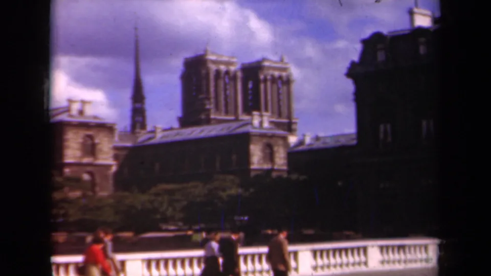 1939 Paris view of people walking by a bridge balustrade, with Notre-Dame towers and riverside buildings behind them.
