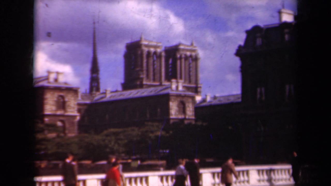 1939 Paris frame with Notre-Dame Cathedral centered beyond the bridge, pedestrians below, and dark building edges framing the view.