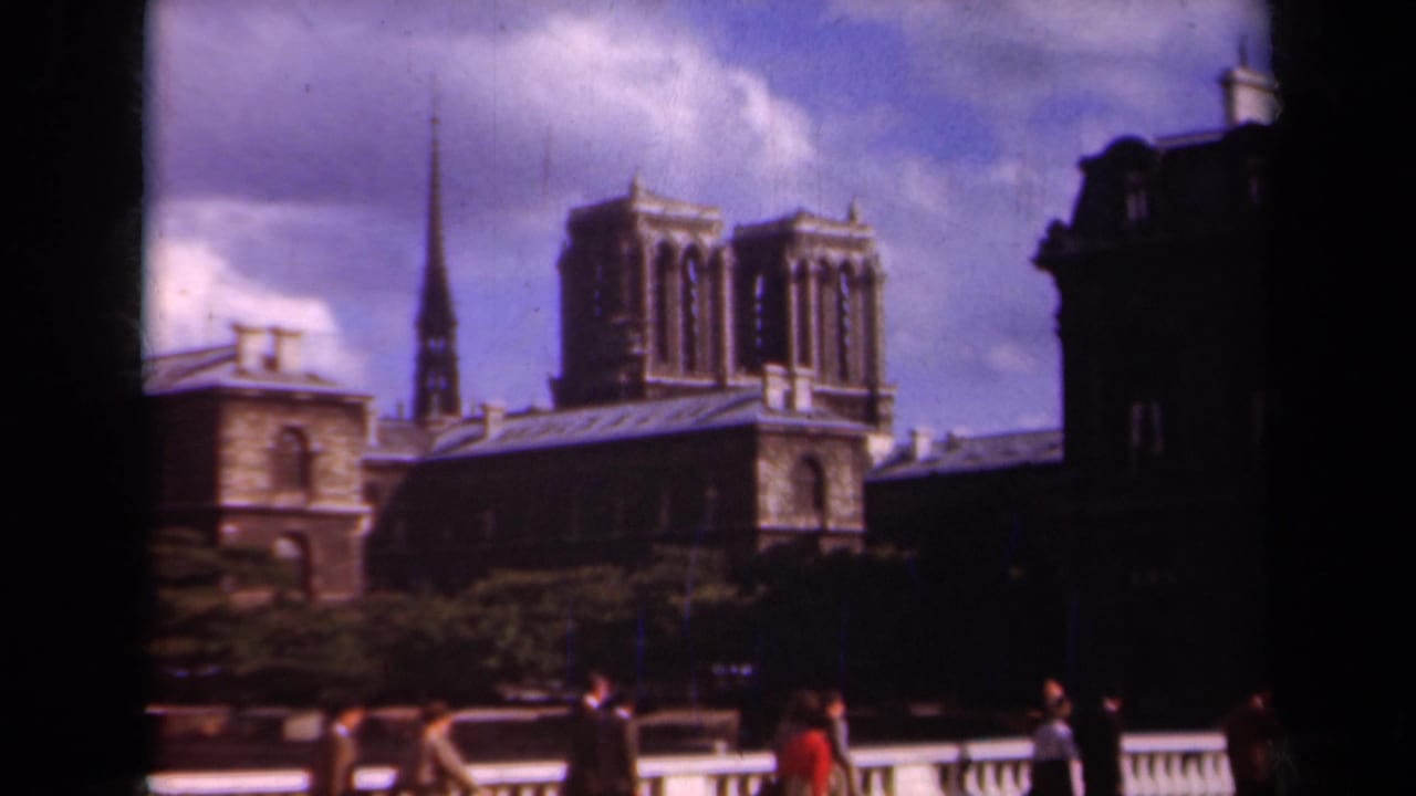 1939 Paris home-movie frame showing Notre Dame from across a bridge, with pedestrians, trees, and cloudy sky.