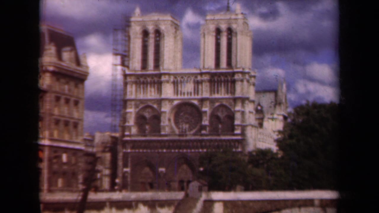 1939 Paris frame centered on Notre Dame's facade, with scaffolding at the left tower and heavy clouds above.