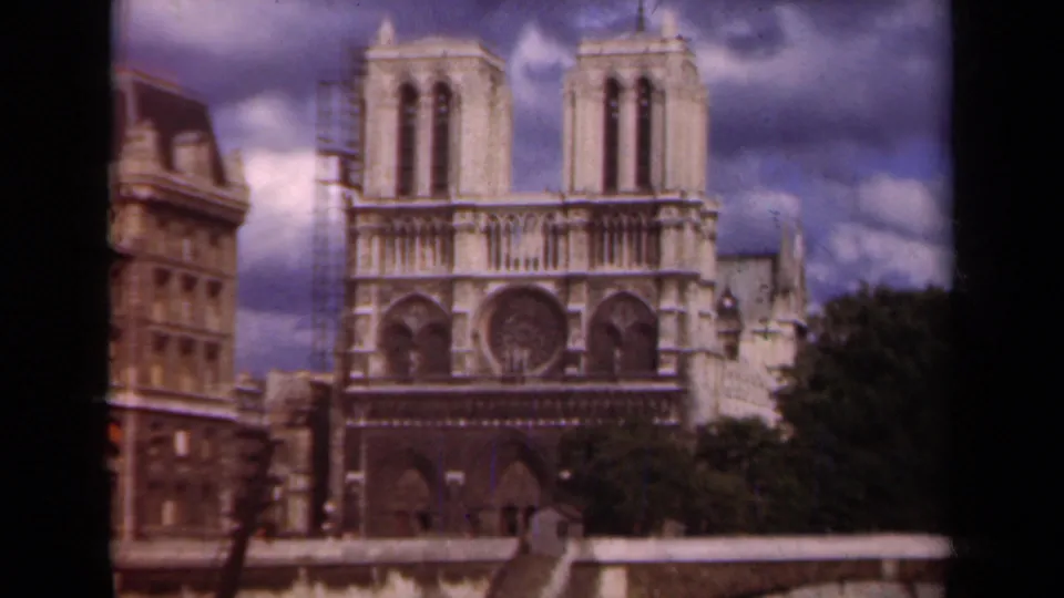 1939 Paris frame centered on Notre Dame's facade, with scaffolding at the left tower and heavy clouds above.