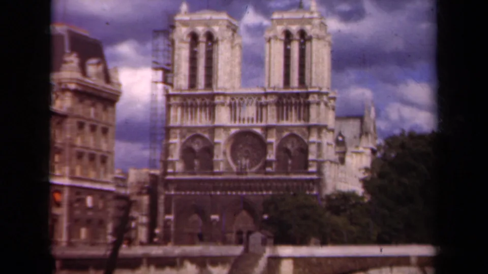 1939 Paris frame showing Notre Dame's Gothic facade, scaffolding on one side, nearby buildings, and trees.