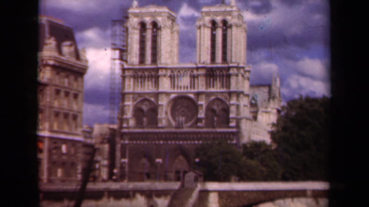 1939 Paris 8mm frame showing Notre-Dame Cathedral across the river, with left-tower scaffolding and a cloudy sky above the facade.