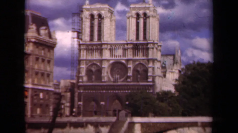 1939 Paris 8mm frame showing Notre-Dame Cathedral across the river, with left-tower scaffolding and a cloudy sky above the facade.