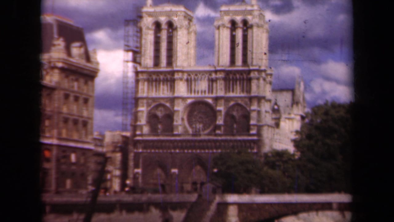 1939 Paris 8mm frame showing Notre Dame Cathedral's west facade, twin towers, rose window, and nearby riverside buildings.