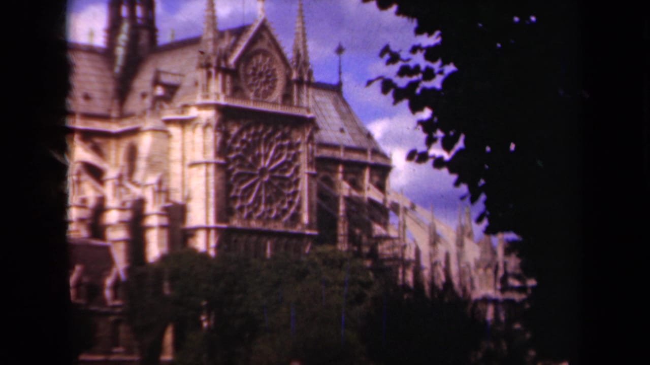 1939 Paris 8mm frame showing Notre Dame Cathedral from the side, with rose window, spires, roofline, and dark tree framing.