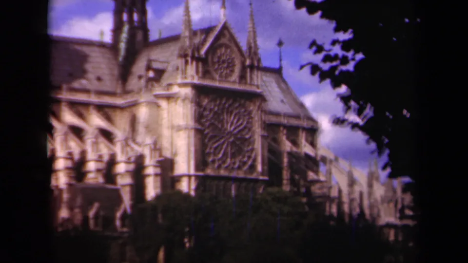 1939 Paris 8mm frame of Notre Dame Cathedral's side elevation, showing the rose window, spires, roof, trees, and warm faded color.