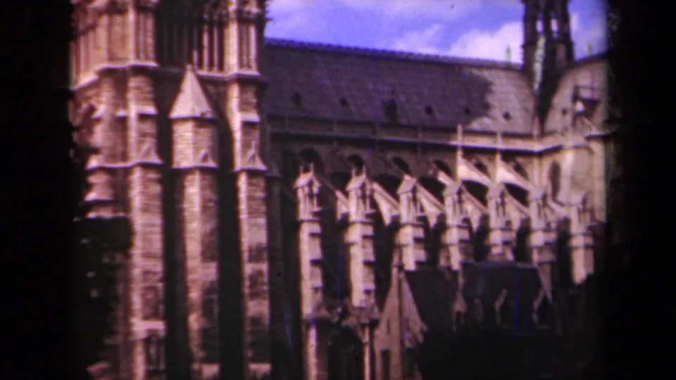 1939 Paris home-movie frame of Notre-Dame's side stonework, Gothic buttresses, roofline, and tower edge.