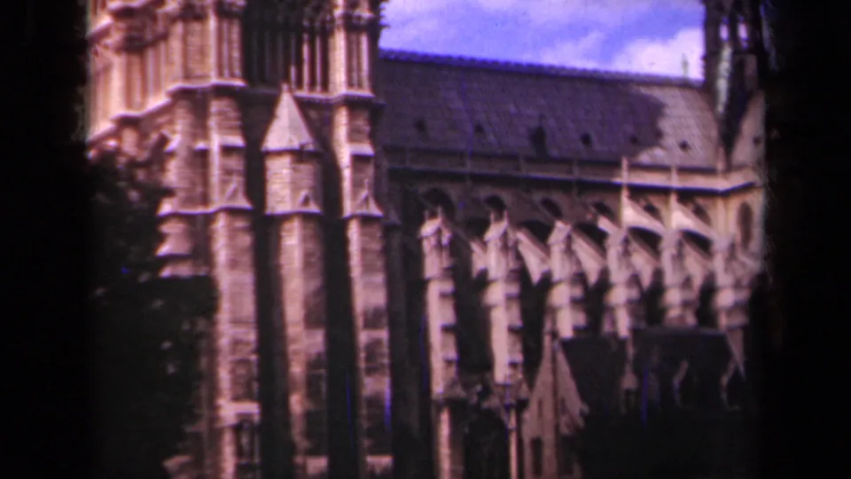 1939 Paris home-movie frame showing Notre-Dame Cathedral's Gothic exterior, with tower details, buttresses, trees, and blue sky.