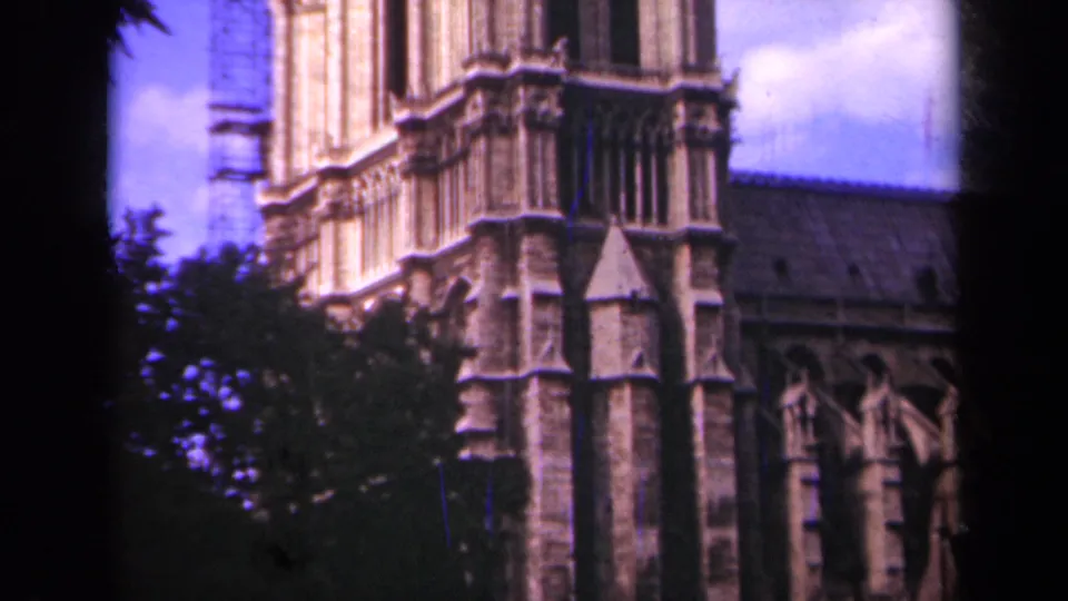 1939 Paris home-movie still showing a closer Notre-Dame tower view, with Gothic stonework, nearby trees, roofline, and scaffolding visible.