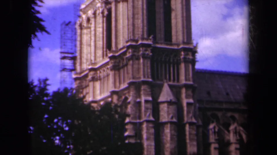 1939 Paris frame showing Notre-Dame Cathedral tower details, scaffolding, trees, roofline, blue sky, and rounded 8mm film borders.