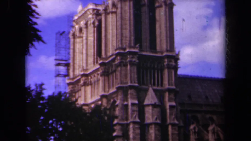 1939 Paris 8mm frame showing Notre-Dame Cathedral's upper stone facade with scaffolding at left and tree silhouettes around the view.