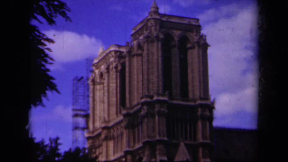 1939 Paris 8mm view looking up at Notre-Dame Cathedral's upper tower, with side scaffolding, arched openings, clouds, and tree silhouettes.